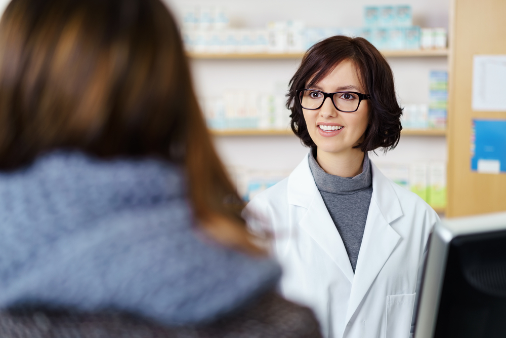 Young Female Pharmacist Talking to a Customer at the Counter Pleasantly.
