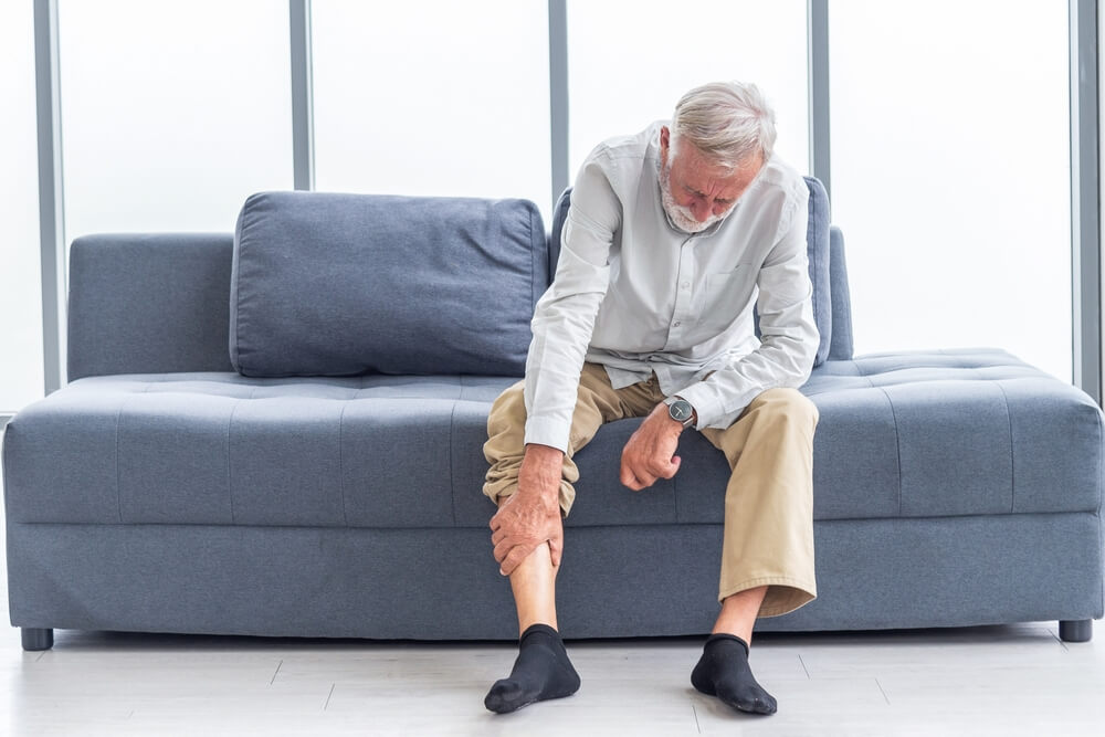 Älterer Mann mit Schmerzen in den Beinen auf dem Sofa